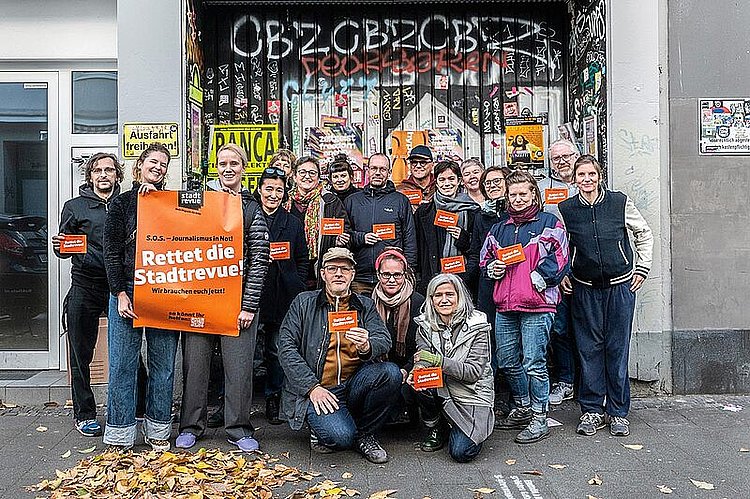 2024: Die Mitarbeiter:innen des Stadtrevue-Verlags stehen vor dem Tor des Verlagshauses an der Maastrichter Straße und halten ein Plakat mit der Aufschrift "Rettet die Stadtrevue"